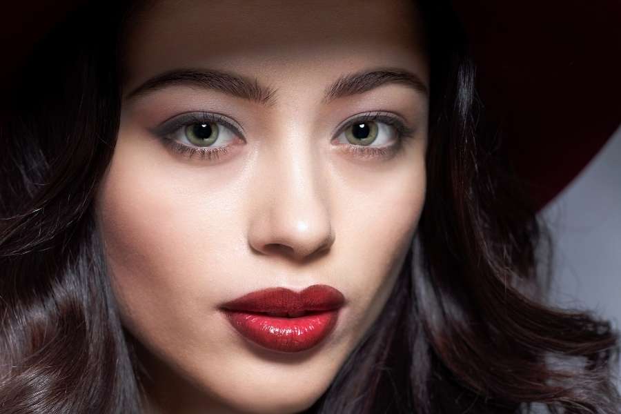 Une femme brune portant un rouge à lèvres rouge intense et un maquillage de soirée glamour.